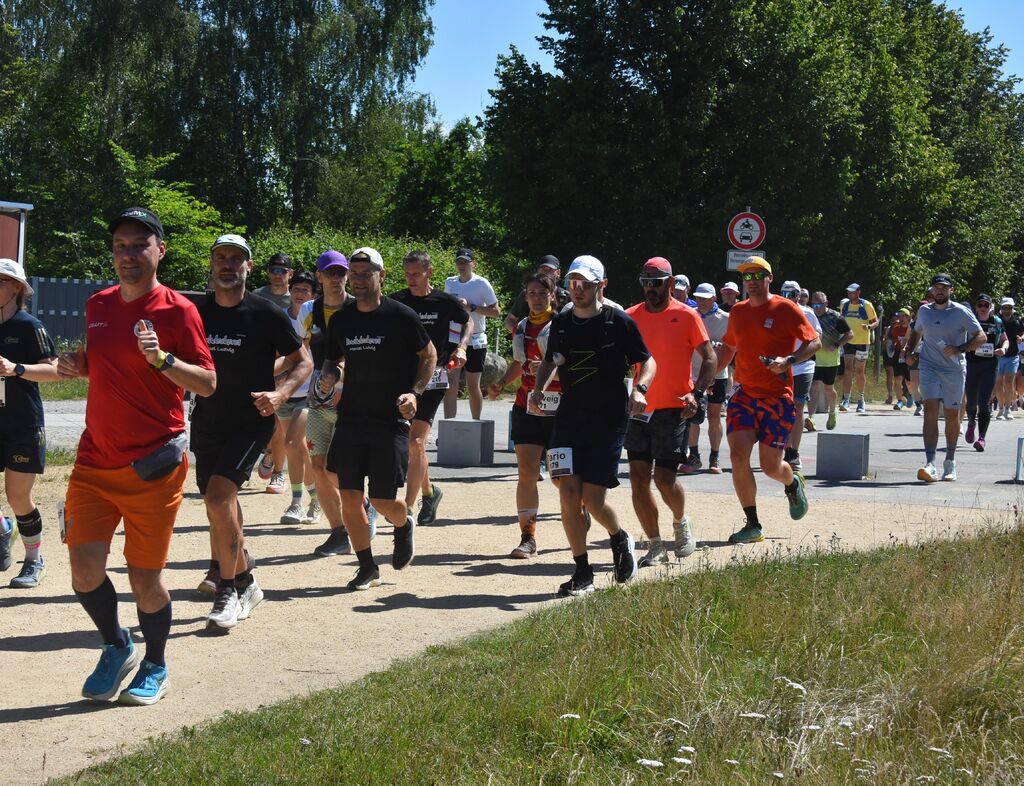 Foto einer gr&ouml;&szlig;eren L&auml;ufergruppe beim O-SEE Backyard Ultra 2026 bei Sonnenschein